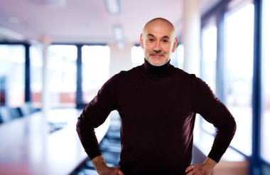 Toplantı odasında dikilip kameraya bakan kendinden emin orta yaşlı bir adam. Orta yaşlı erkek günlük kıyafetler giyiyor. Ellerini göğsüne koy.. 