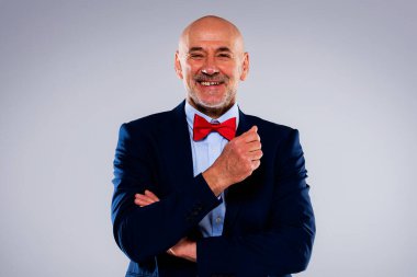 Tecrit edilmiş arka planda duran yaşlı adamın stüdyo portresi. Uzayı kopyala Kendine güvenen, takım elbiseli, kırmızı papyonlu ve kameraya gülen bir erkek..