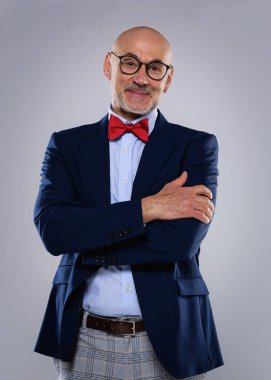 Tecrit edilmiş arka planda duran yaşlı adamın stüdyo portresi. Uzayı kopyala Takım elbiseli, kırmızı papyonlu ve kameraya gülümseyen kendinden emin bir erkek..