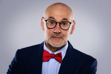 Tecrit edilmiş arka planda duran son sınıf öğrencisinin yakın çekimi. Uzayı kopyala Takım elbiseli, kırmızı papyonlu ve kameraya gülümseyen kendinden emin bir erkek..