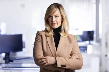 Ofiste kendine güvenen, sarı saçlı bir kadın var. Gülümseyen iş kadını iş kıyafeti giyiyor..