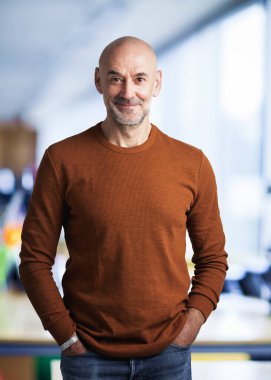 Ofiste duran orta yaşlı kel adam. Kendine güvenen iş adamı kazak giyiyor ve kameraya gülümsüyor..