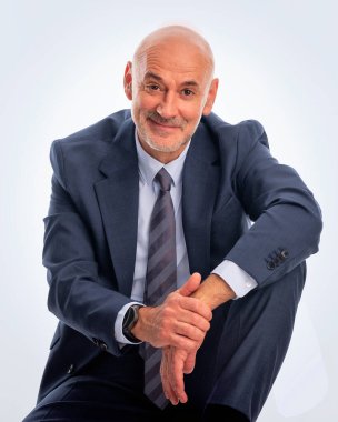 İzole edilmiş beyaz arka planda oturan gülümseyen bir adamın stüdyo portresi. Kendine güvenen erkek takım elbiseli ve kameraya gülümsüyor. Yakın plan çekim. Boşluğu kopyala.