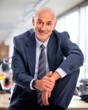 İdari işadamı ofiste oturuyor. Kendine güvenen erkek takım elbiseli ve kameraya gülümsüyor. Yakın çekim.. 