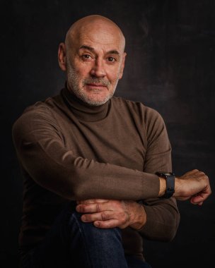 Esmer arka planda orta yaşlı bir adamın stüdyo portresi. Sakallı kel adam. Belini kaldır, boğazlı kazak. Uzayı kopyala Koyu arkaplan. 