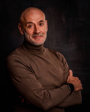 Esmer arka planda orta yaşlı bir adamın stüdyo portresi. Sakallı kel adam. Belini kaldır, boğazlı kazak. Uzayı kopyala Koyu arkaplan. 