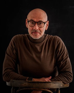 Esmer arka planda orta yaşlı bir adamın stüdyo portresi. Sakallı kel adam. Belini kaldır, gözlük tak. Uzayı kopyala Koyu arkaplan. 