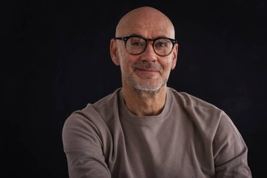 Esmer arka planda orta yaşlı bir adamın stüdyo portresi. Sakallı kel adam. Belini kaldır, gözlük tak. Uzayı kopyala Koyu arkaplan. 