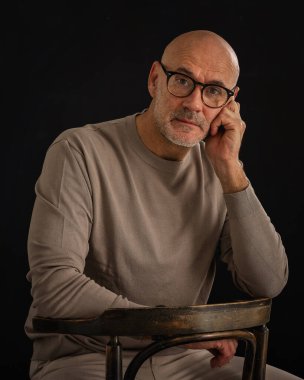 Düşünceli, orta yaşlı, gözlüklü ve sıradan kıyafetler giyen bir adamın stüdyo fotoğrafı. Kendine güvenen bir erkek kameraya bakıyor ve derin düşünce ve karar verme mekanizmasını öneriyor. Boşluğu kopyala. 