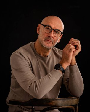 Düşünceli, orta yaşlı, gözlüklü ve sıradan kıyafetler giyen bir adamın stüdyo fotoğrafı. Kendine güvenen bir erkek kameraya bakıyor ve derin düşünce ve karar verme mekanizmasını öneriyor. Boşluğu kopyala. 