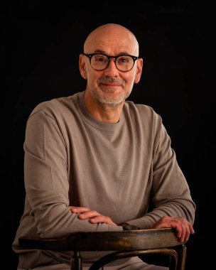 Düşünceli, orta yaşlı, gözlüklü ve sıradan kıyafetler giyen bir adamın stüdyo fotoğrafı. Kendinden emin bir erkek kameraya bakıyor ve gülümsüyor. İzole edilmiş arka plan. Boşluğu kopyala. 