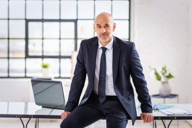 Ofisinde oturmuş kameraya bakan kendinden emin orta yaşlı bir işadamı. Profesyonel erkek takım elbiseli.. 