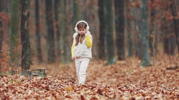 ホワイトヘッドフォンの女の子が秋の公園の公園を歩き — ストック動画