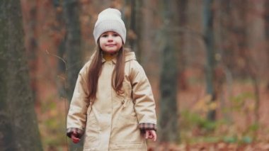 Küçük kız sonbahar ormanında yürüyor.