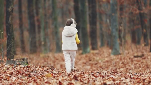 在秋天的公园里 一个戴着白色耳机的女孩走在公园里 — 图库视频影像