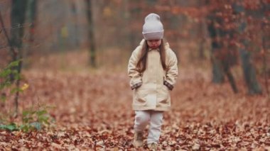 Küçük kız sonbahar ormanında yürüyor.