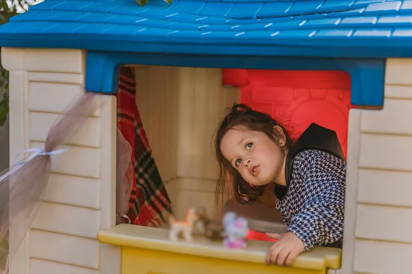 girl is playing in her little house, looking out the door