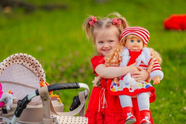 The girl plays with a doll in nature, holding her in her arms