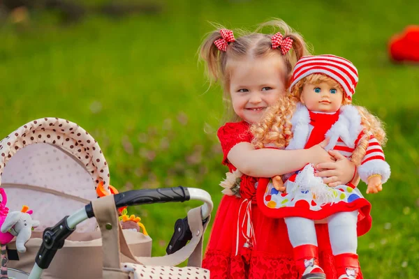 女の子は自然に人形と遊ぶ 彼女の腕の中で彼女を保持 — ストック写真