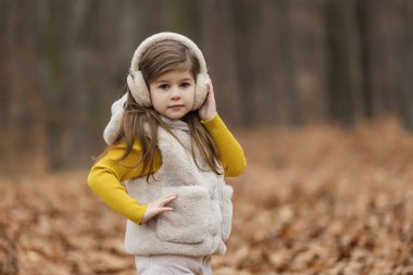 little girl in headphones walks through the autumn forest