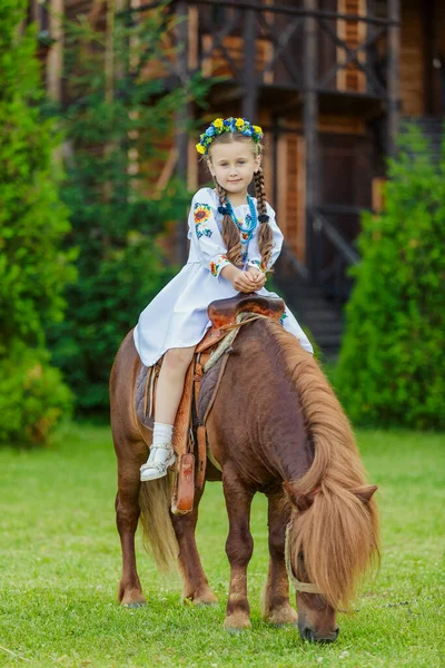 ウクライナの民族衣装の少女が芝生の上でポニーに乗る — ストック写真