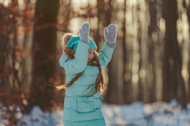 Güneşle aydınlatılan bir kış ormanının arka planında bir kızın portresi