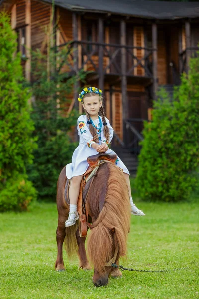 一个身穿乌克兰民族服装的小女孩骑着小马在草坪上 — 图库照片