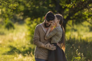 Kız erkek arkadaşının kulağına bir şey söylüyor, doğada yürüyor.