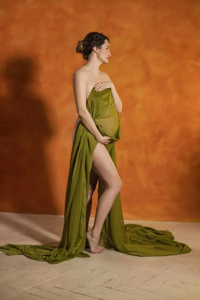 Беременная Женщина Оранжевом Фоне Покрытая Зеленой Тканью — стоковое фото