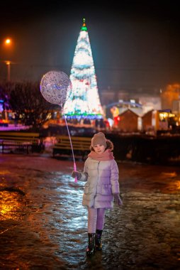 Kız, şehrin arka planına karşı Akşamları büyük bir yılbaşı ağacı