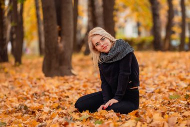 Sarı saçlı ve gözlüklü bir kız sonbahar parkında oturuyor.