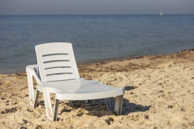 Denizin arka planında beyaz plastik şezlong