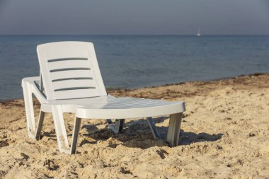 Denizin arka planında beyaz plastik şezlong