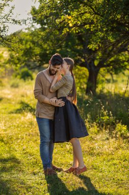 Kız erkek arkadaşının kulağına bir şey söylüyor, doğada yürüyor.