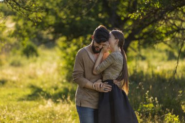 Kız erkek arkadaşının kulağına bir şey söylüyor, doğada yürüyor.