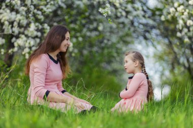 Anne ve kızı çiçek açan bir elma bahçesinde yürüyorlar.