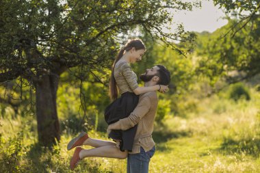 Adam yaz parkında kız arkadaşını kollarında taşıyor.