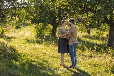 Genç çift, arka planda güneşle aydınlanmış, doğada kucaklaşıyorlar.