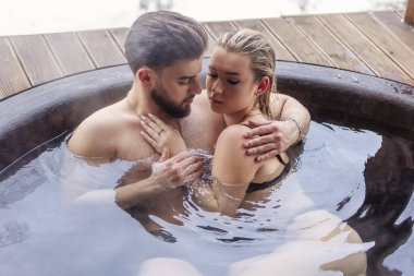 Genç çift büyük bir küvette otururken birbirlerine sarılıyorlar.