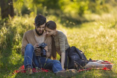 Genç çift doğada dinleniyor ve kameradaki fotoğraflara bakıyor.