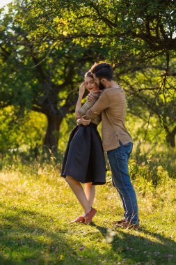Genç çift, arka planda güneşle aydınlanmış, doğada kucaklaşıyorlar.