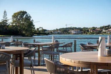 Portekiz, Quinta do Lago 'da bulunan Ria Formosa bölgesinde bir göl kenarındaki bir sahil barından masa ve sandalyeler..