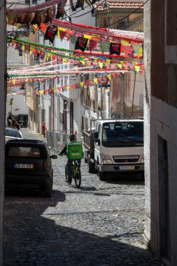 LISBON, PORTUGAL - 28 HAZİRAN 2022: Lizbon 'da dar bir kaldırım taşı caddesinde giden bir Uber Eats bisiklet teslimatçısı görülüyor.