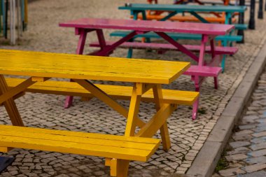 Bir kaldırım taşı caddesindeki birkaç renkli ahşap masanın yakın görüntüsü.