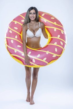 Gri arkaplanı üzerinde şişme yüzme halkası olan bikinili bir kadın..