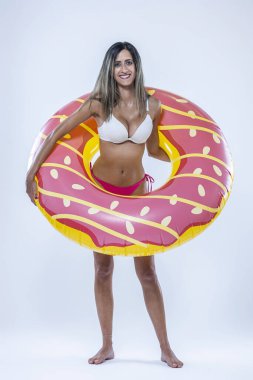 Gri arkaplanı üzerinde şişme yüzme halkası olan bikinili bir kadın..