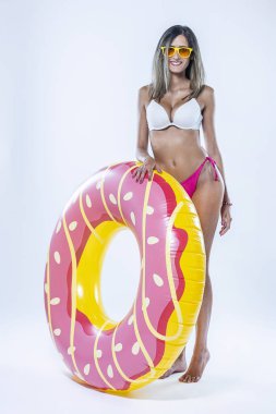 Gri arkaplanı üzerinde şişme yüzme halkası olan bikinili bir kadın..