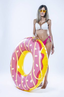 Gri arkaplanı üzerinde şişme yüzme halkası olan bikinili bir kadın..