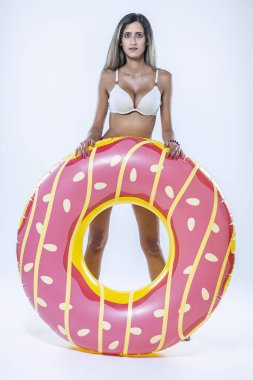 Gri arkaplanı üzerinde şişme yüzme halkası olan bikinili bir kadın..