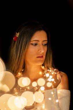 Genç bir kadın farklı pozlarda siyah bir arkaplanda Noel 'in sicim ışıklarını tutuyor..